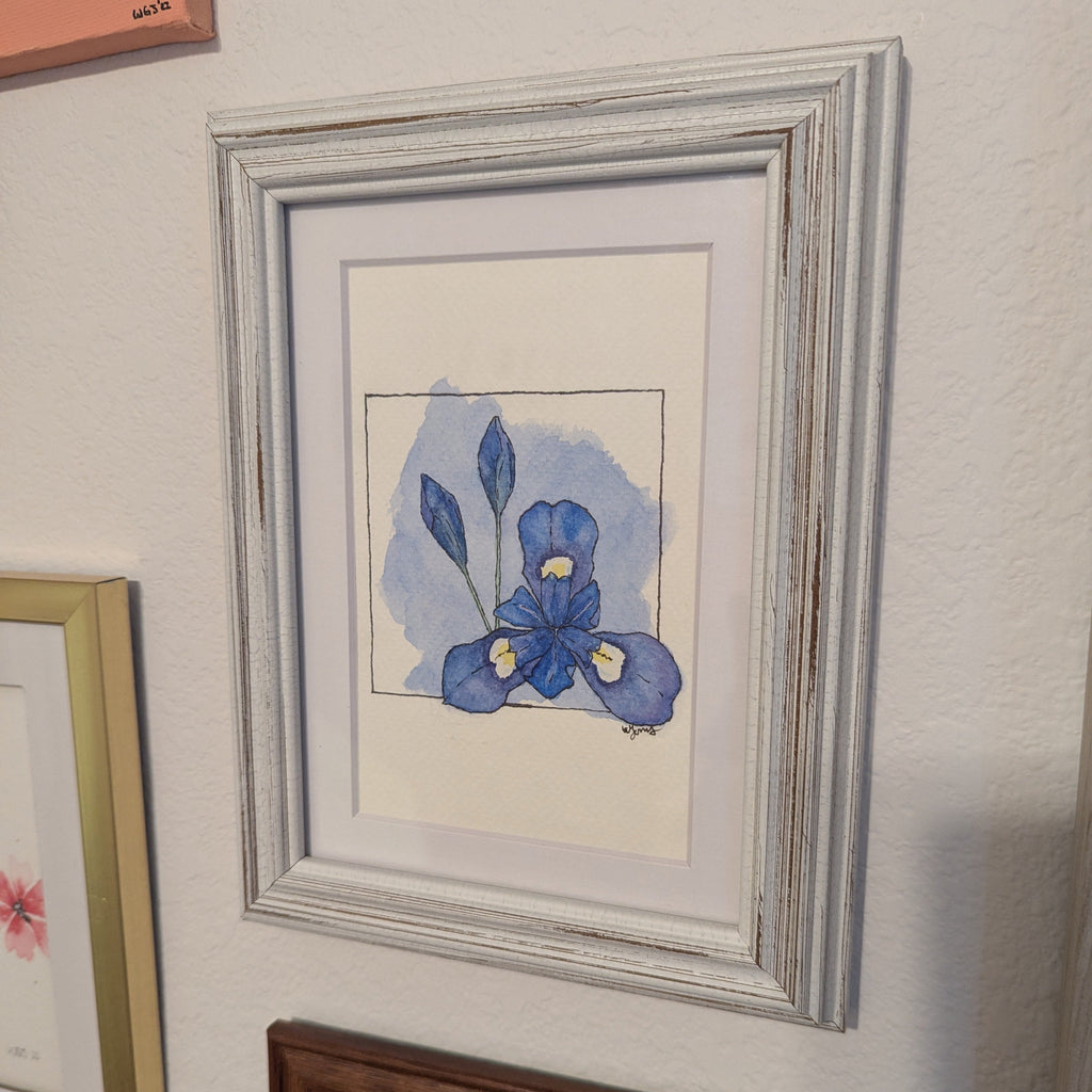 Framed artwork of a blue flower on a wall with other framed pieces.