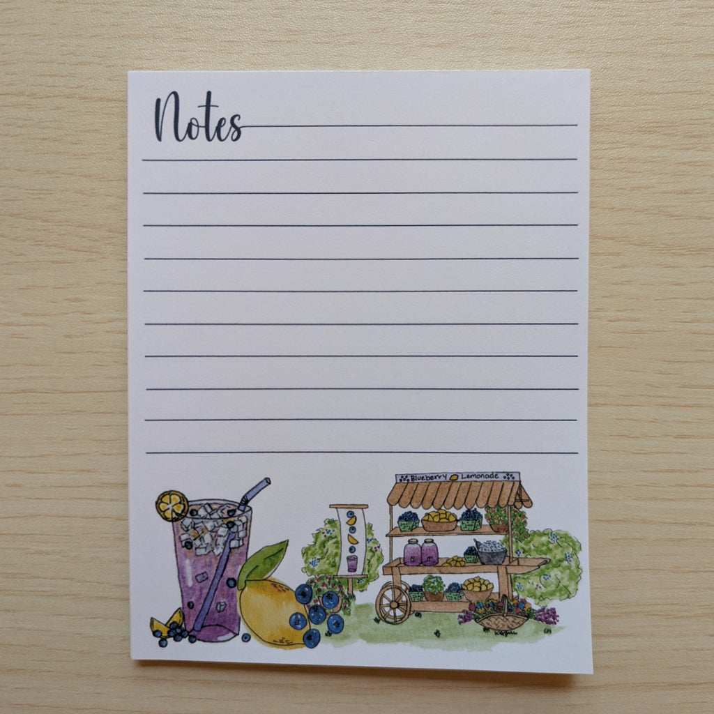 A white lined notepad with the word 'Notes' at the top left and a small watercolor illustration along the bottom, placed on a light wood surface.