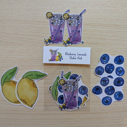 A sticker pack containing illustrated lemon slices, blueberry drinks with straws, and blueberries, displayed on a light wood background with a small label reading 'Blueberry Lemonade Sticker Pack'.