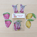 A sticker pack featuring watermelon slices, lemons, and pink lemonade illustrations arranged on a light wood background with a small label reading 'Watermelon Lemonade Sticker Pack'.