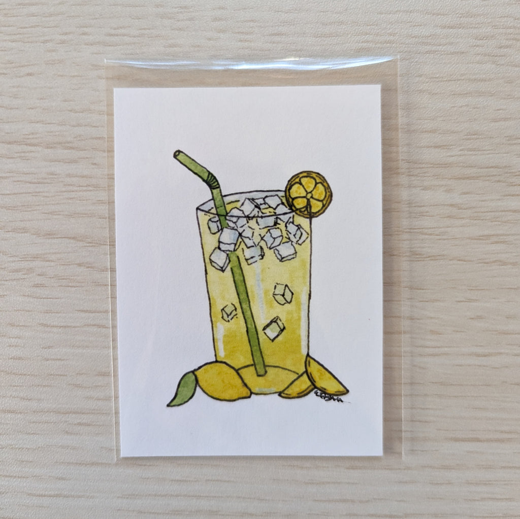A square white ACEO size art print featuring a hand-drawn illustration of a lemonade glass with ice, a green straw, yellow lemon slices, and a green leaf, photographed on a light wood surface.