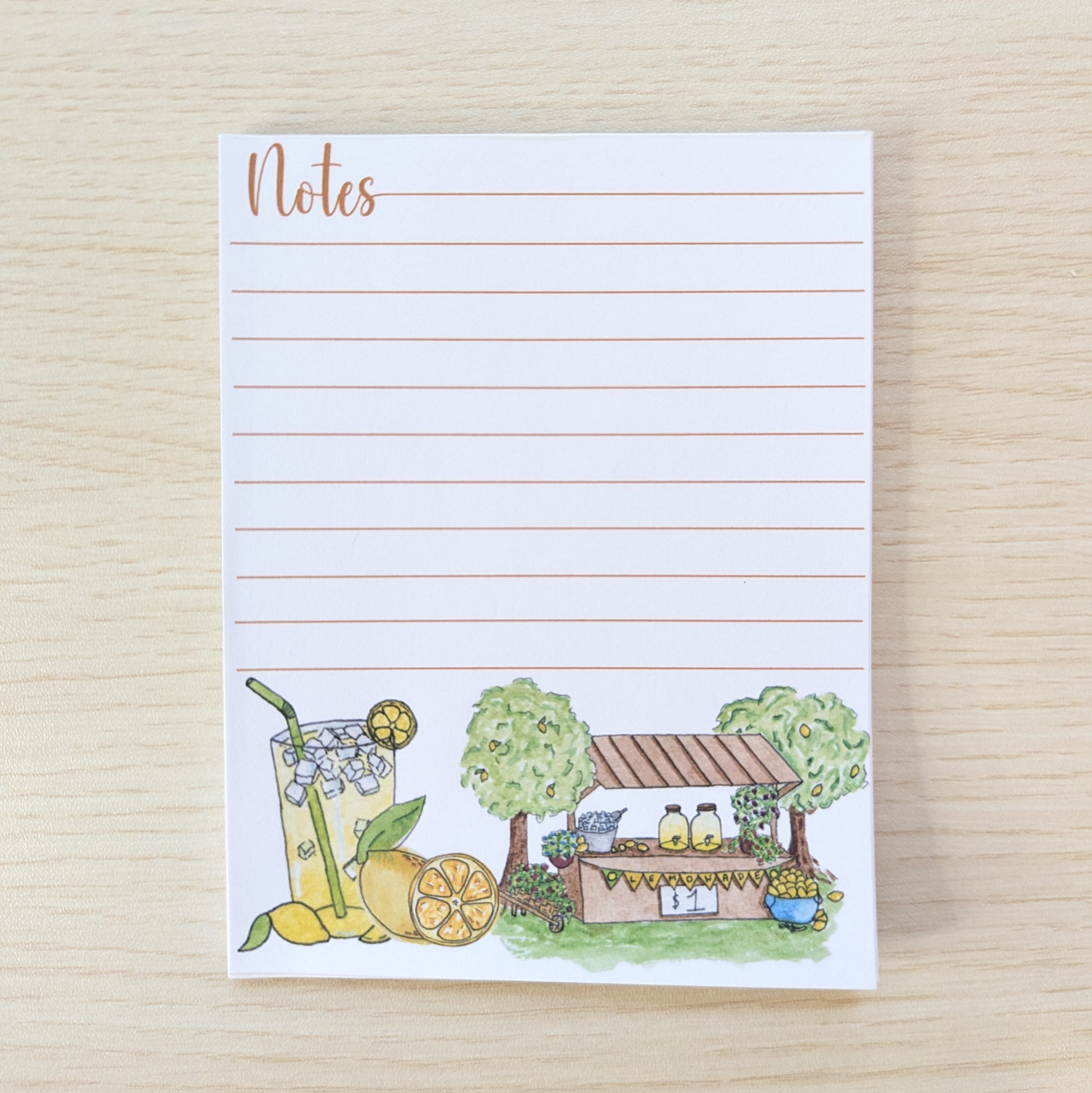 A lined notepad with the word 'Notes' at the top and a small illustrated lemonade stand and drink at the bottom, photographed on a light wood surface.